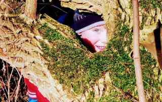 Kind schaut durch Lücke in bemoostem Baum